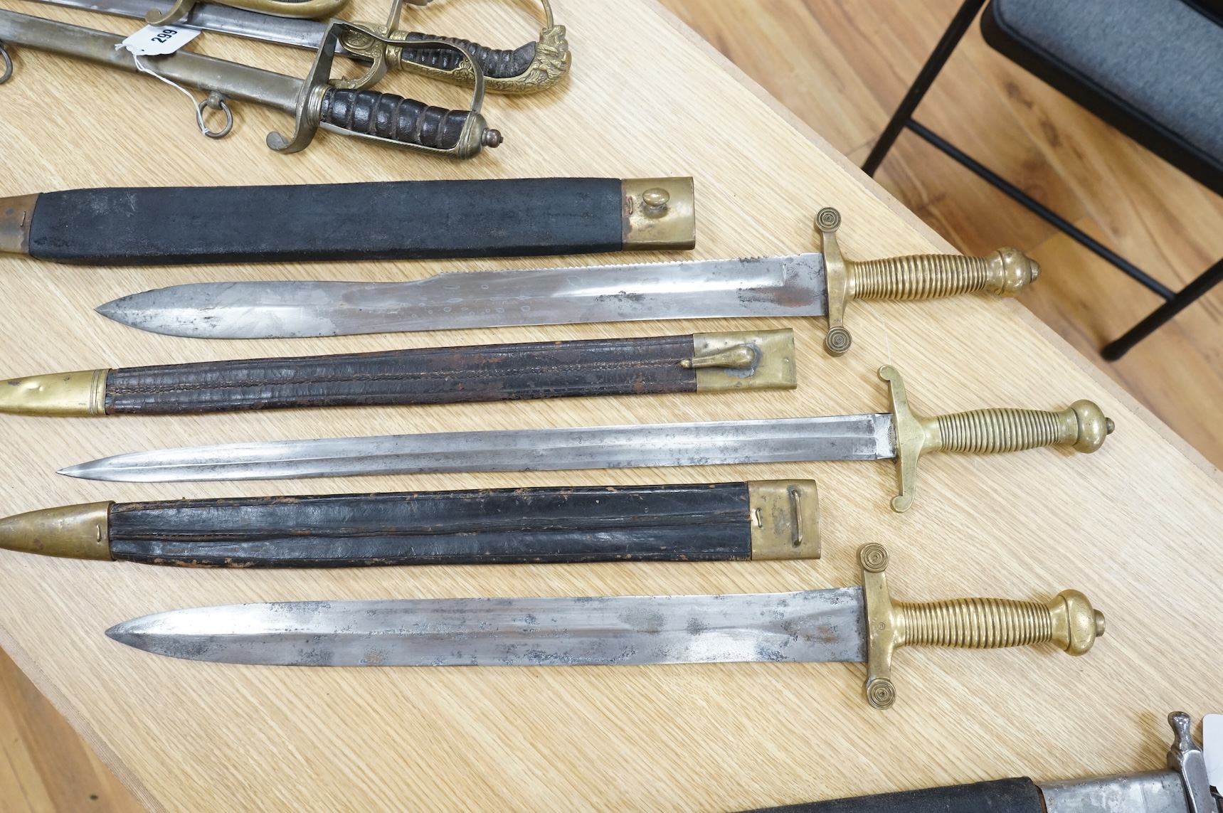 Three Continental infantry officer’s sidearms briquette, the first stamped Paris, in its brass mounted leather scabbard, another similar with sawback blade (illegible stamp), and another similar with thin blade, stamped